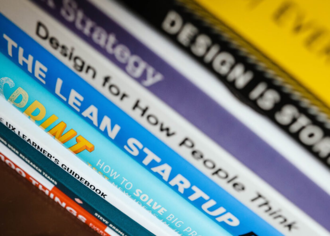 Närbild av flera diagonalt staplade böcker med synliga titlar relaterade till design, strategi, nystartade företag och problemlösning, bl.a. DESIGN, Design for How People Think och THE LEAN STARTUP.