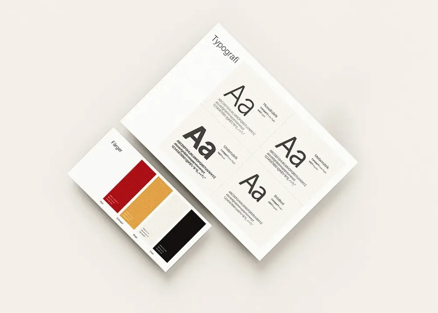 Två designark ligger på en ljus yta: det ena visar färgprover i rött, gult och svart; det andra visar olika teckenstorlekar och stilar, märkta med typografiska detaljer.
